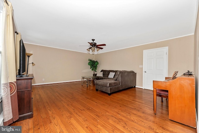 living room featuring crown molding, light wood-style flooring, baseboards, and ceiling fan