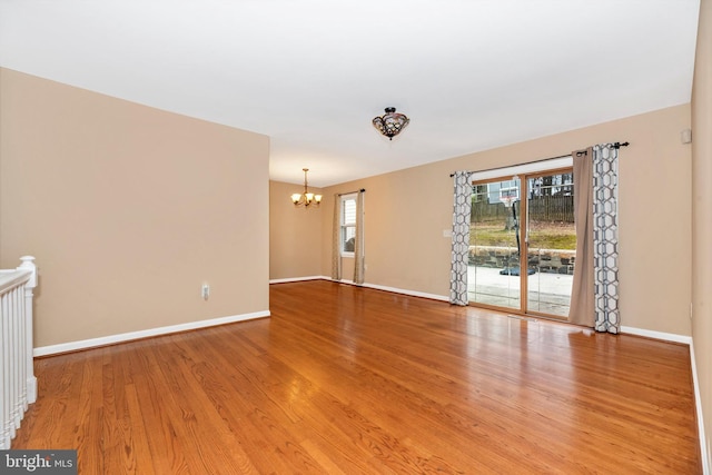 unfurnished living room with an inviting chandelier, wood finished floors, and baseboards