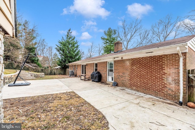 view of side of property featuring brick siding, a chimney, a patio, and fence