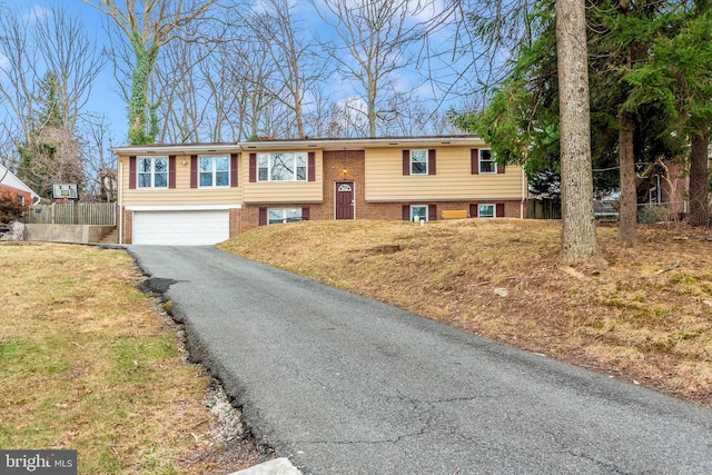 split foyer home with aphalt driveway, fence, a front yard, a garage, and brick siding