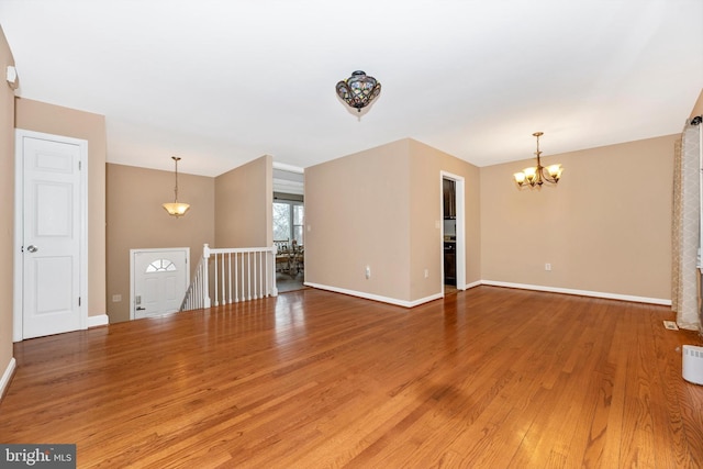 unfurnished living room featuring baseboards, light wood finished floors, and a chandelier