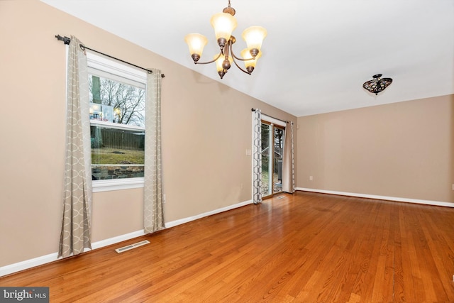 spare room with visible vents, baseboards, wood finished floors, and a chandelier