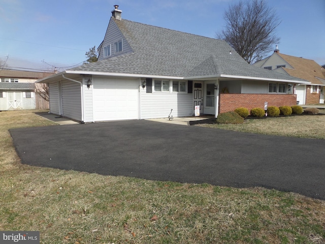 view of front of house with roof with shingles, a chimney, a front lawn, a garage, and aphalt driveway