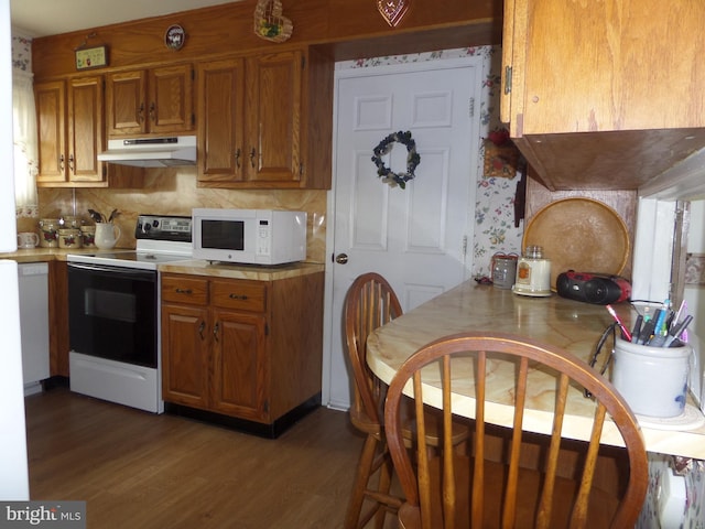 kitchen featuring under cabinet range hood, white appliances, brown cabinetry, and dark wood-type flooring