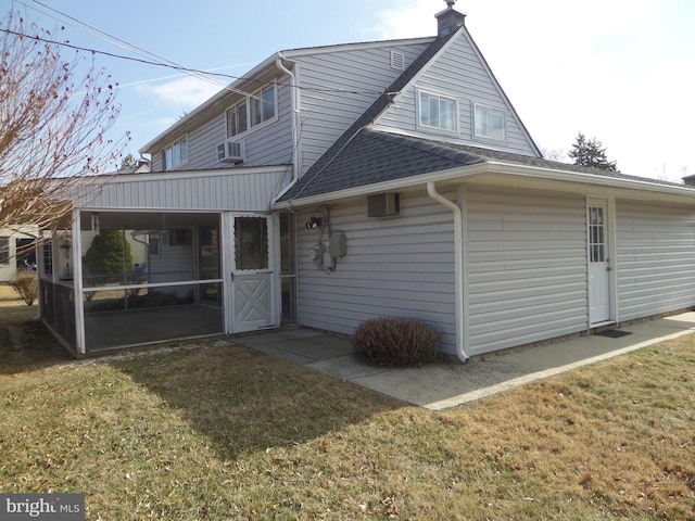 rear view of house featuring a lawn, a sunroom, cooling unit, a shingled roof, and a chimney