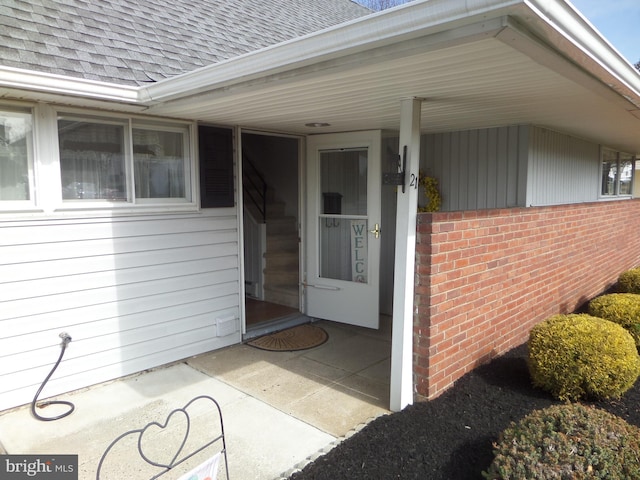 view of exterior entry with brick siding and roof with shingles