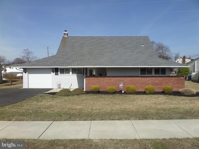 view of front facade with aphalt driveway, an attached garage, a chimney, and a front lawn