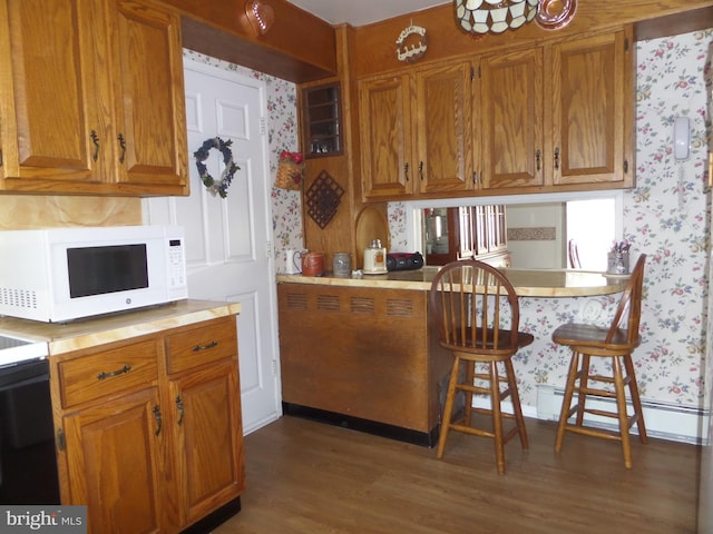 kitchen featuring baseboard heating, wood finished floors, brown cabinetry, wallpapered walls, and white microwave