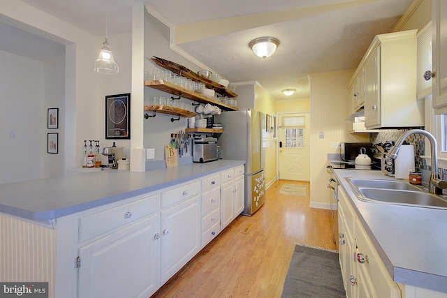 kitchen with freestanding refrigerator, white cabinetry, a peninsula, light wood-type flooring, and under cabinet range hood