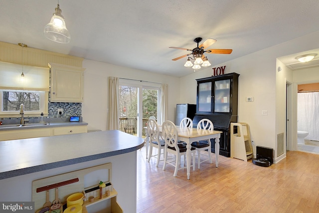 kitchen with visible vents, decorative backsplash, light wood-style floors, pendant lighting, and a sink