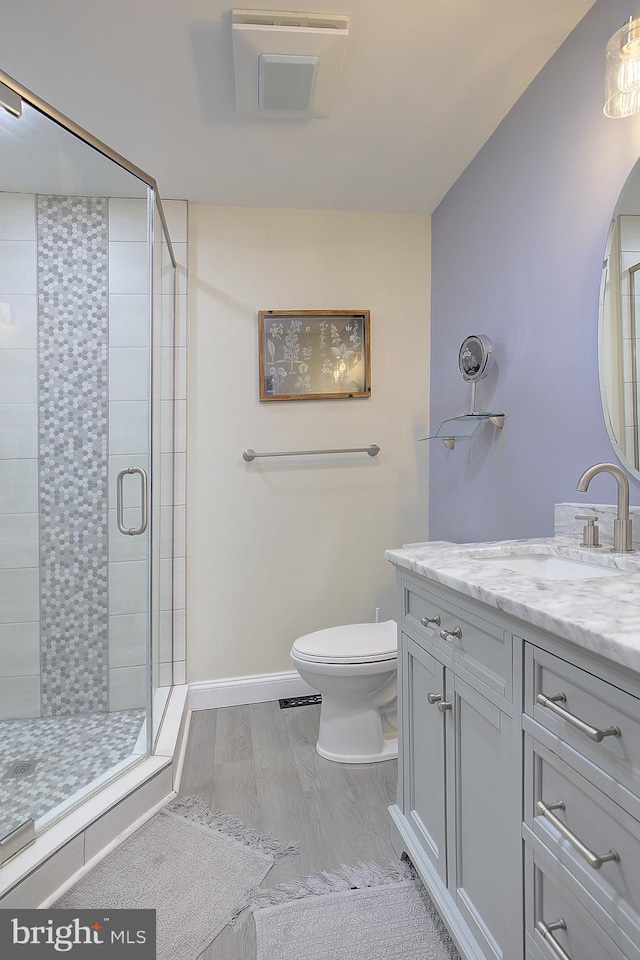 bathroom with toilet, wood finished floors, vanity, baseboards, and a stall shower