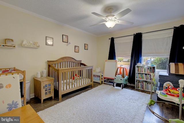 bedroom featuring ornamental molding, a nursery area, a textured ceiling, and wood finished floors