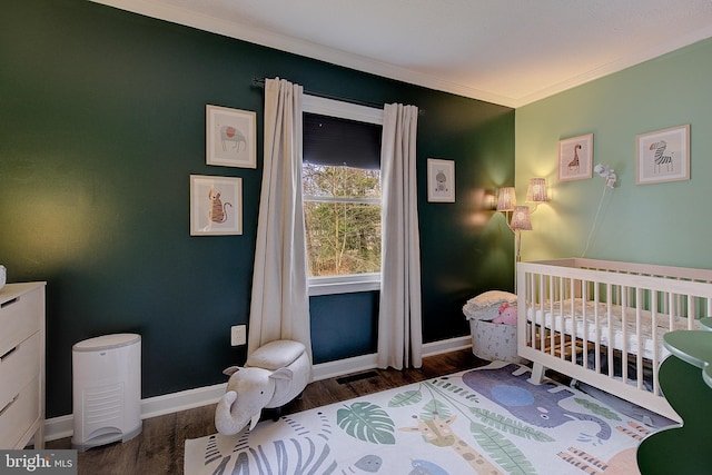 bedroom featuring ornamental molding, a nursery area, baseboards, and wood finished floors