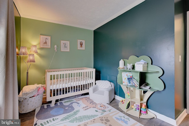 bedroom featuring baseboards, a crib, wood finished floors, and crown molding