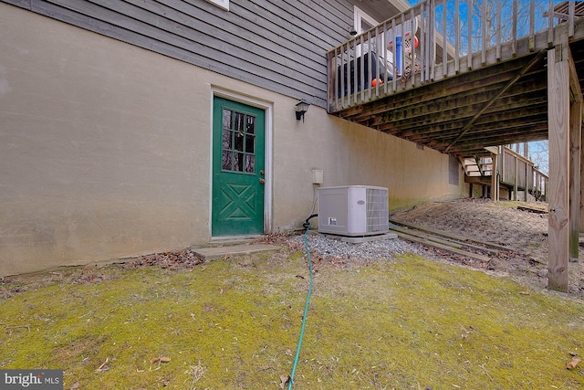 entrance to property featuring a yard, central AC unit, and stucco siding