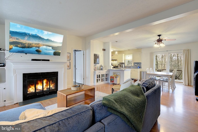 living room with ceiling fan, light wood-type flooring, and a fireplace with flush hearth