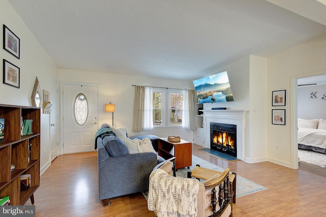 living area featuring a fireplace with flush hearth, baseboards, and wood finished floors