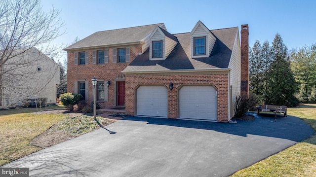 view of front of property with brick siding, a chimney, an attached garage, a front yard, and driveway