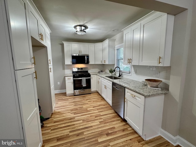 kitchen with decorative backsplash, light wood-style flooring, appliances with stainless steel finishes, white cabinetry, and a sink