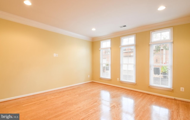 spare room with ornamental molding, plenty of natural light, wood finished floors, and visible vents