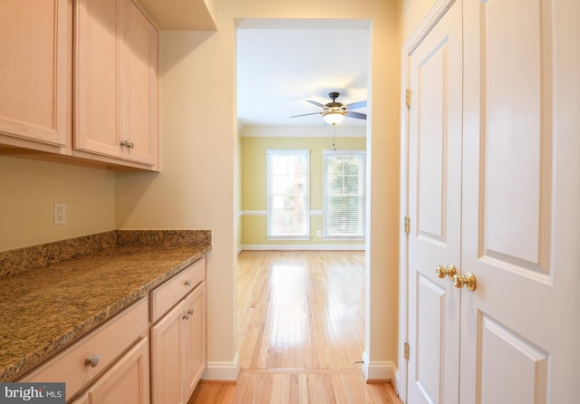 kitchen with stone counters, crown molding, light wood-style flooring, a ceiling fan, and baseboards