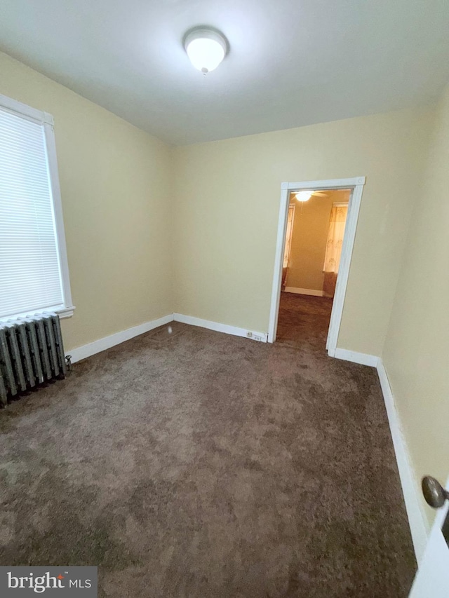 carpeted empty room featuring baseboards and radiator