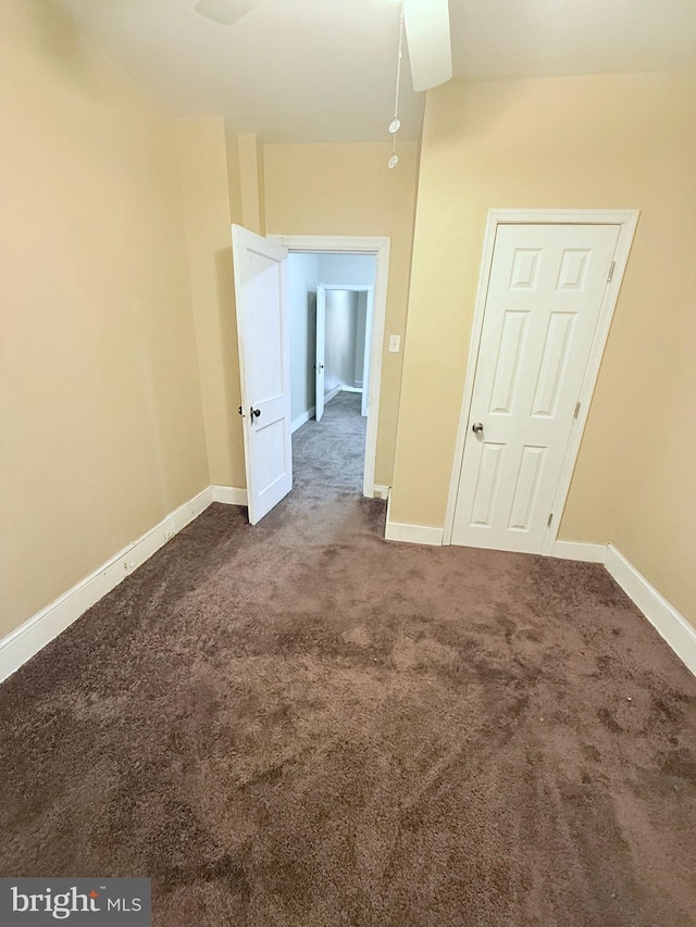 unfurnished room with baseboards and dark carpet