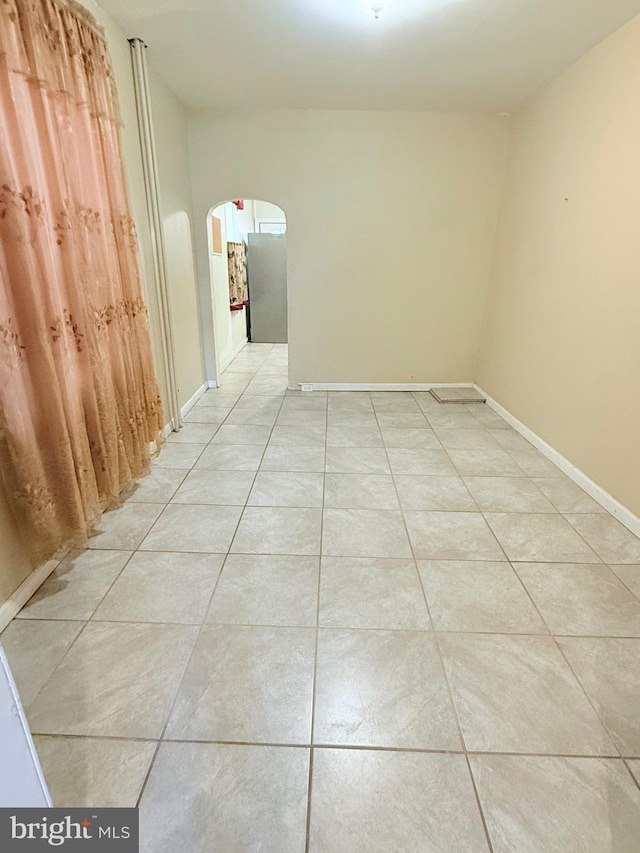 spare room featuring arched walkways, light tile patterned flooring, and baseboards