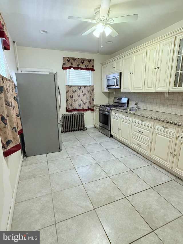 kitchen featuring light tile patterned floors, radiator heating unit, stainless steel appliances, and cream cabinetry