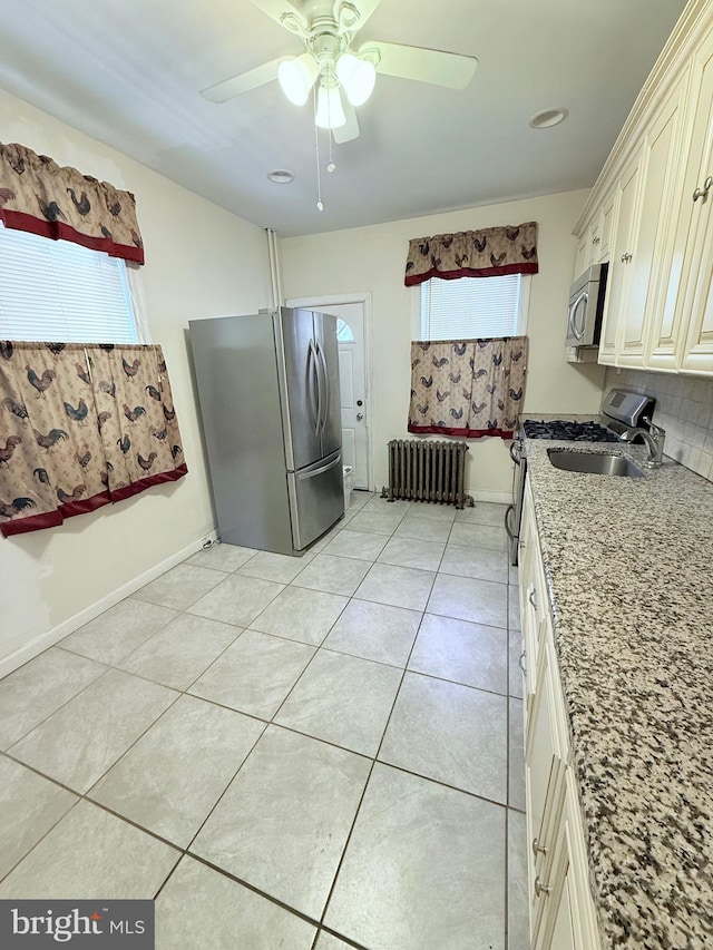 kitchen featuring a ceiling fan, radiator, light stone countertops, stainless steel appliances, and light tile patterned flooring