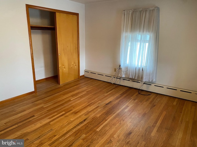 unfurnished bedroom with a baseboard heating unit, wood-type flooring, a closet, and baseboards