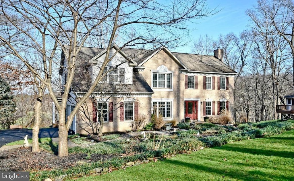 colonial-style house with brick siding, a chimney, and a front yard