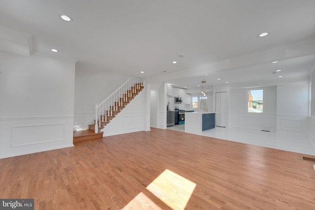 unfurnished living room with light wood-type flooring, a sink, recessed lighting, a decorative wall, and stairs