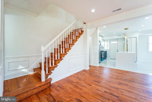 stairs with visible vents, ornamental molding, wood finished floors, wainscoting, and a decorative wall