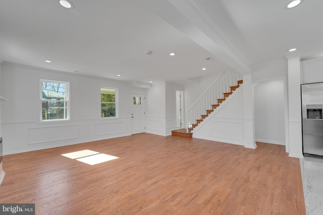 unfurnished living room featuring light wood finished floors, stairway, recessed lighting, and a decorative wall