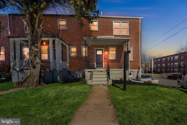 view of property featuring a yard, covered porch, and brick siding