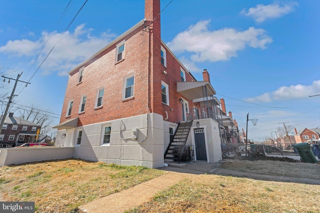 rear view of house featuring stairway, brick siding, a chimney, and fence