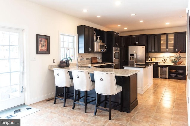 kitchen with wine cooler, stainless steel appliances, a sink, a center island, and decorative backsplash