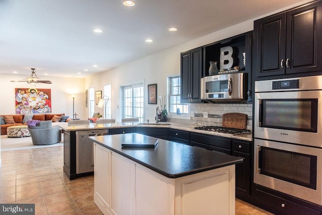 kitchen with decorative backsplash, appliances with stainless steel finishes, a center island, a peninsula, and a sink