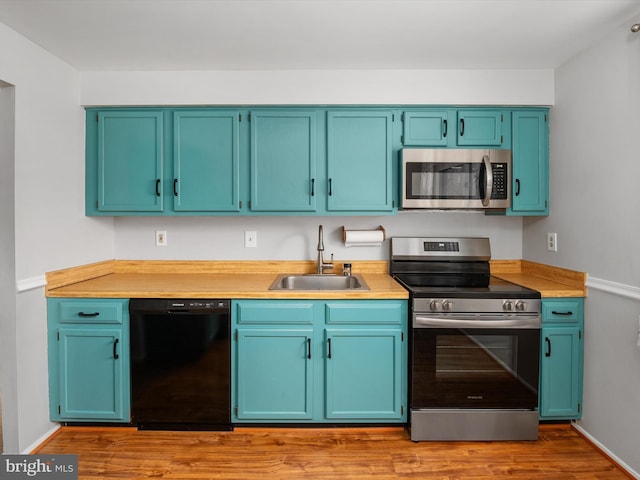 kitchen with light wood finished floors, appliances with stainless steel finishes, light countertops, and a sink