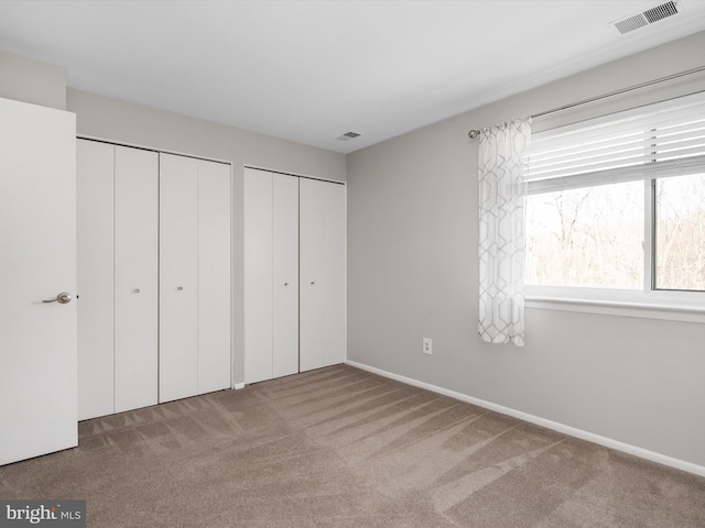 unfurnished bedroom with visible vents, two closets, and carpet flooring