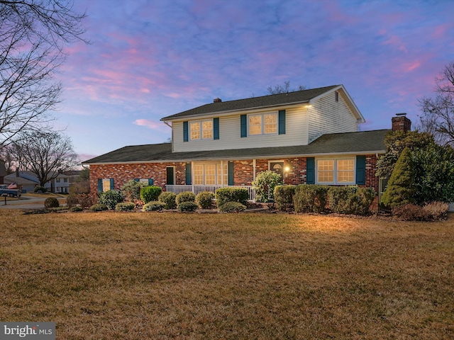 traditional-style home featuring a porch, a lawn, brick siding, and a chimney