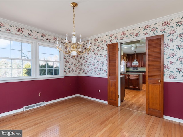 unfurnished dining area featuring visible vents, wallpapered walls, light wood-style floors, and a wainscoted wall