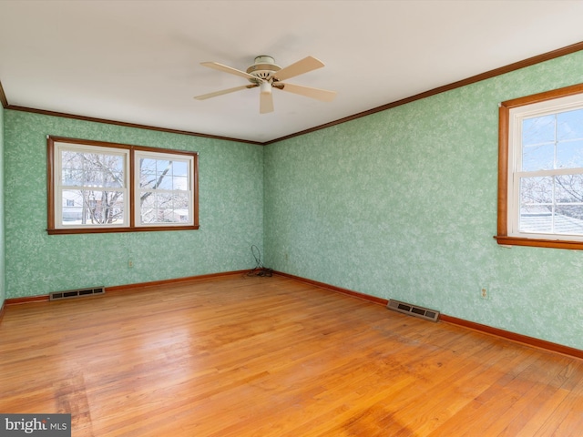 empty room with visible vents, wallpapered walls, light wood-style floors, and ornamental molding