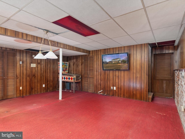 finished below grade area with carpet flooring, wood walls, and a drop ceiling