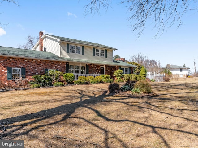 view of front of property with fence, covered porch, brick siding, and a chimney