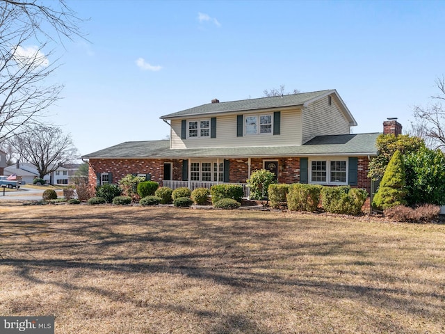 traditional-style house featuring a front lawn, a porch, brick siding, and a chimney