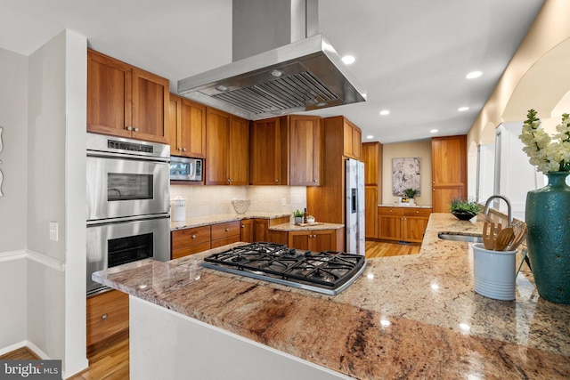 kitchen featuring light stone counters, a sink, stainless steel appliances, tasteful backsplash, and island range hood