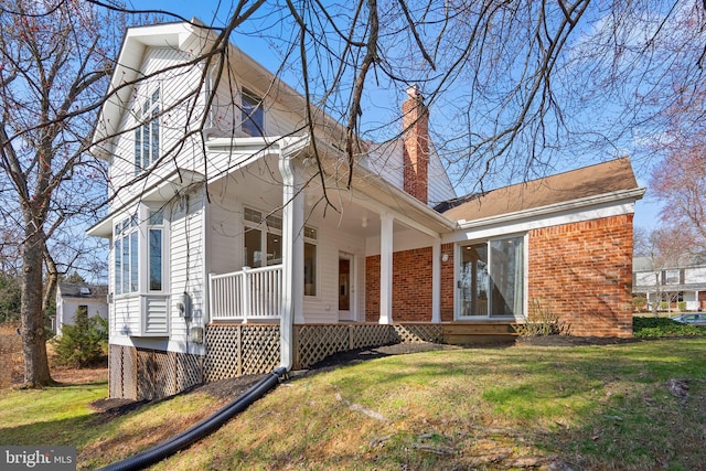 view of front of house with a chimney, brick siding, a porch, and a front yard