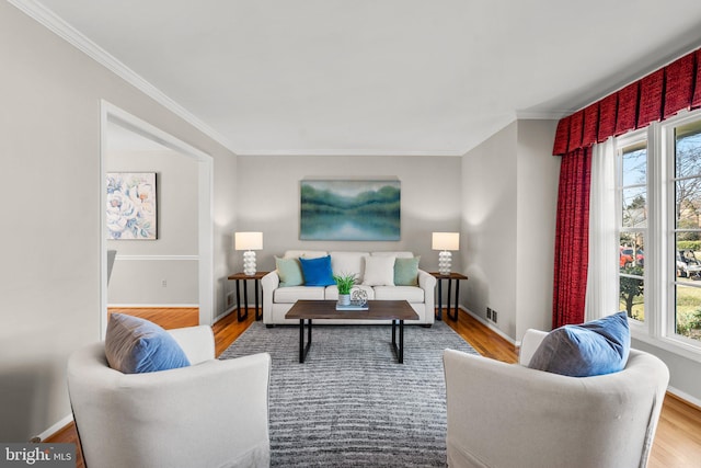 living room with crown molding, wood finished floors, visible vents, and baseboards